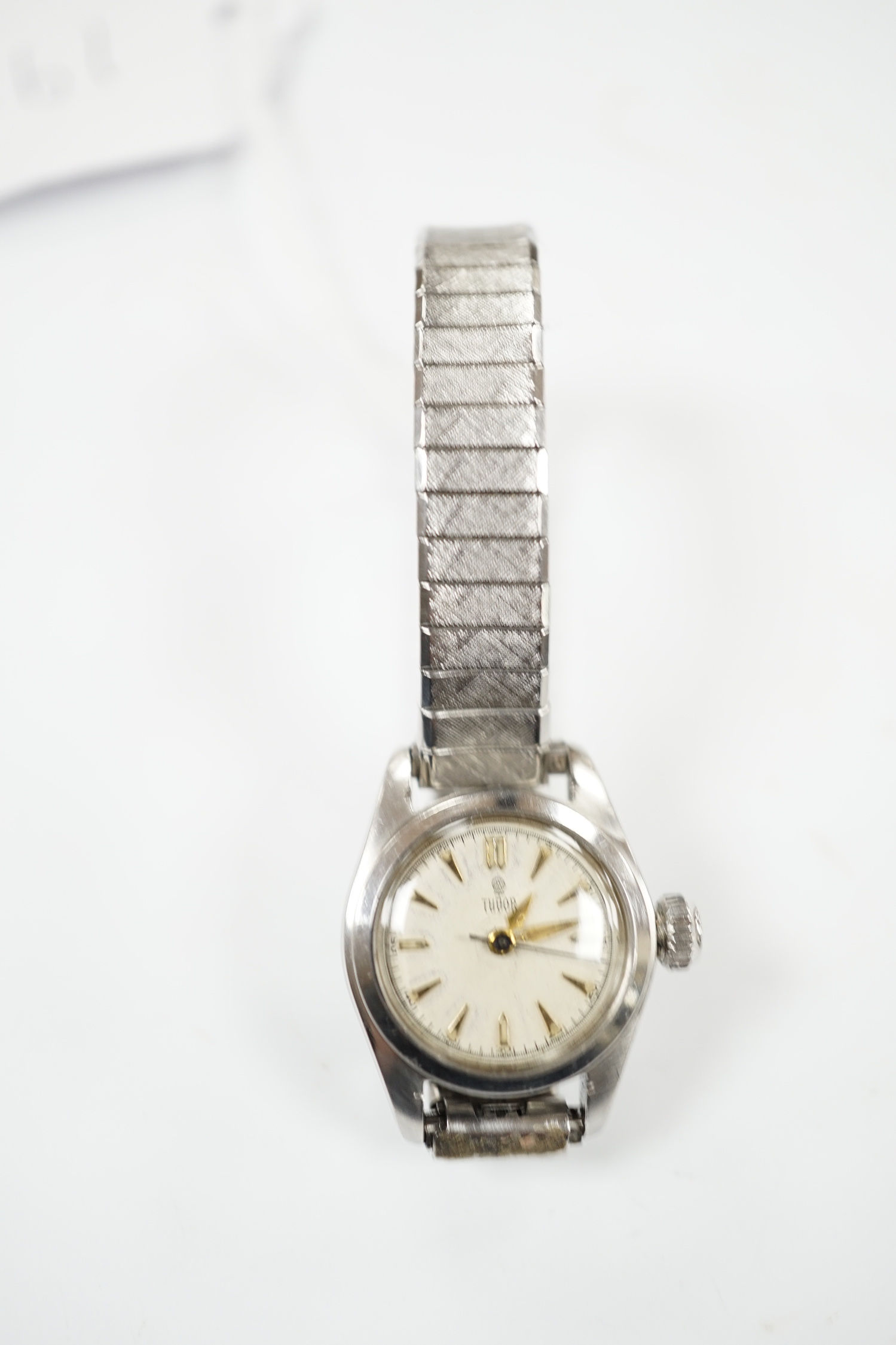A lady's stainless steel Tudor manual wind wrist watch, with baton numerals, on an associated flexible bracelet.
